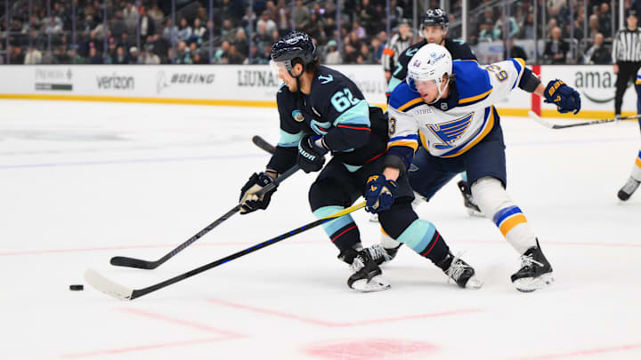 Apr 12, 2025; Seattle, Washington, USA; Seattle Kraken defenseman Brandon Montour (62) plays the puck while defended by St. Louis Blues left wing Jake Neighbours (63) during overtime at Climate Pledge Arena. Mandatory Credit: Steven Bisig-Imagn Images