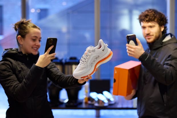A man and a woman take pictures of white Nike shoes.