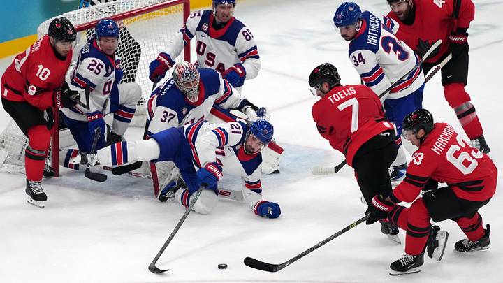 Feb 22, 2026; Milan, Italy; Dylan Larkin (21) and Connor Hellebuyck (37) of the United States battle for the puck against Devon Toews (7) and Brad Marchand (63) of Canada during the men's ice hockey gold medal game during the Milano Cortina 2026 Olympic Winter Games at Milano Santagiulia Ice Hockey Arena. Mandatory Credit: James Lang-Imagn Images