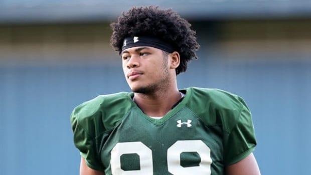 Football player Jonah Laulu gets ready for practice in a green jersey.