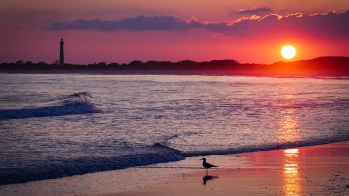 Shore line of Cape May, New Jersey with a lighthouse in the background and sun setting.