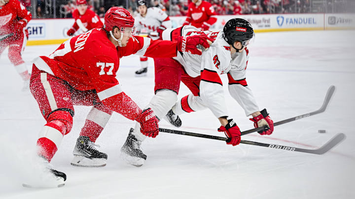 Apr 4, 2025; Detroit, Michigan, USA; Detroit Red Wings defenseman Simon Edvinsson (77) and Carolina Hurricanes center Jesperi Kotkaniemi (82) battle for the puck during the third period at Little Caesars Arena. Mandatory Credit: Tim Fuller-Imagn Images