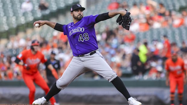 Senzatela throwing a ball in grey pants against the Orioles with black socks and a purple jersey out of a black glov