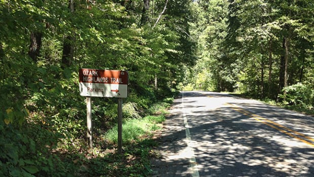 A sign for the Ozark Highlands Trail located in some trees alongside the road.