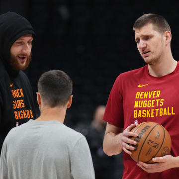 Denver Nuggets center Nikola Jokic (15) (right) and Phoenix Suns center Jusuf Nurkic (20) left speak to Nuggets assistant coach Ognjen Stojakovic before a game at Ball Arena. 