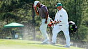 Apr 12, 2024; Augusta, Georgia, USA; Tiger Woods shields himself from sand being blown by strong