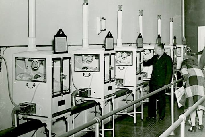 Men and women look at an exhibit of premature babies in incubators.