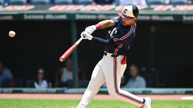 A baseball player wearing a navy jersey, white pants, and a white, navy, and red helmet while hitting a baseball.