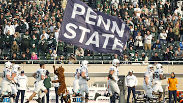 The Penn State Nittany Lion mascot runs with a Penn State flag