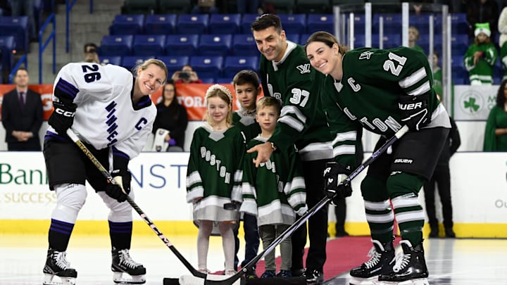 Jan 3, 2024; Lowell, MA, USA; Minnesota forward Kendall Coyne (26) and Boston forward Hilary Knight (21) participate in a ceremonial puck drop with retired Boston Bruins player Patrice Bergeron before a PWHL ice hockey game at Tsongas Center. Mandatory Credit: Brian Fluharty-Imagn Images