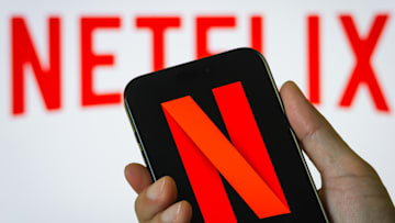 Hand Holding Smartphone Displaying Netflix (NFLX) Logo with Background Branding