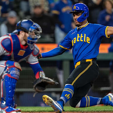 Sep 13, 2024; Seattle, Washington, USA;  Seattle Mariners centerfielder Julio Rodriguez (44) slides safely into home plate to score a run ahead of a tag by Texas Rangers catcher Jonah Heim (28) during the seventh inning at T-Mobile Park. Mandatory Credit: Stephen Brashear-Imagn Images