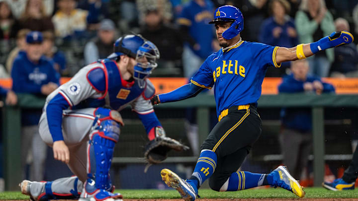 Sep 13, 2024; Seattle, Washington, USA;  Seattle Mariners centerfielder Julio Rodriguez (44) slides safely into home plate to score a run ahead of a tag by Texas Rangers catcher Jonah Heim (28) during the seventh inning at T-Mobile Park. Mandatory Credit: Stephen Brashear-Imagn Images