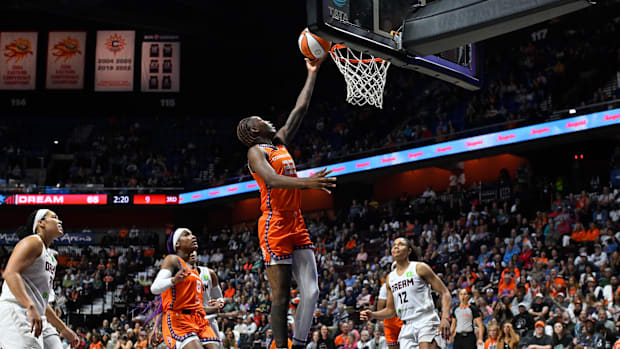 A basketball player in an orange uniforms jumping to a basketball hoop to shoot the ball with players on the court.