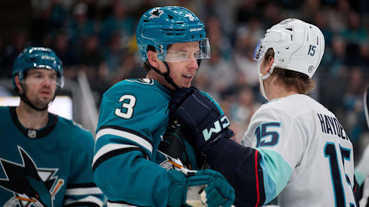 Apr 5, 2025; San Jose, California, USA; Seattle Kraken center John Hayden (15) puts his glove near the face of San Jose Sharks defenseman Henry Thrun (3) during a stoppage of play in the third period at SAP Center at San Jose. Mandatory Credit: Robert Edwards-Imagn Images