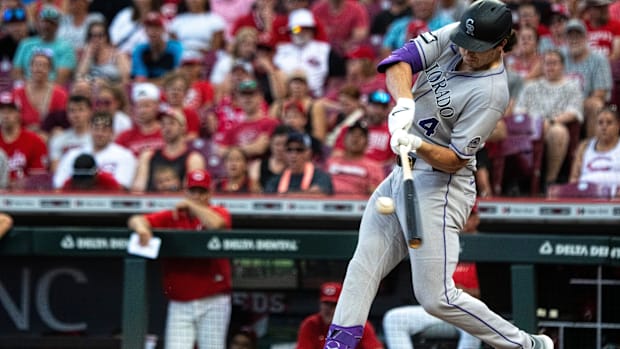 Colorado Rockies player Michael Toglia hits a ball while wearing a black helmet and gray jersey.