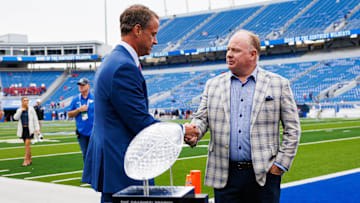 Sep 6, 2025; Lexington, Kentucky, USA; Mississippi Rebels head coach Lane Kiffin (left) greets Kentucky Wildcats head coach Mark Stoops (right) behind the AFCA Coaches Trophy presented by US LBM before the game at Kroger Field. Mandatory Credit: Jordan Prather-Imagn Images