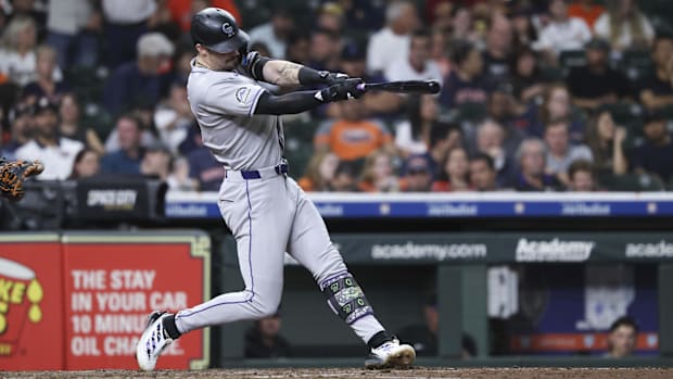 Doyle hitting a white ball in a solid grey uniform with a black arm sleeve and black bat wearing a black ha