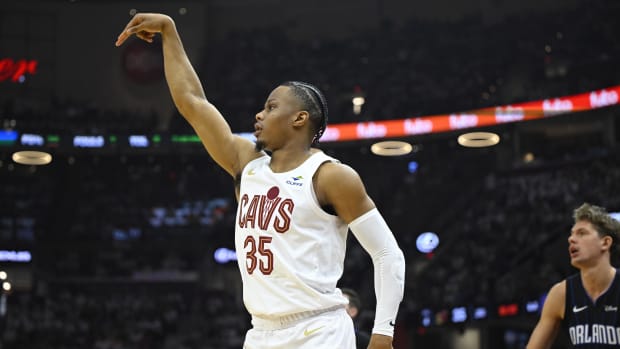 A basketball player wearing a white jersey, white shorts, and a white arm sleeve while shooting a basketball.