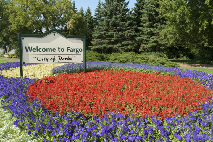 "Welcome to Fargo" sign next to purple and red flower bed.