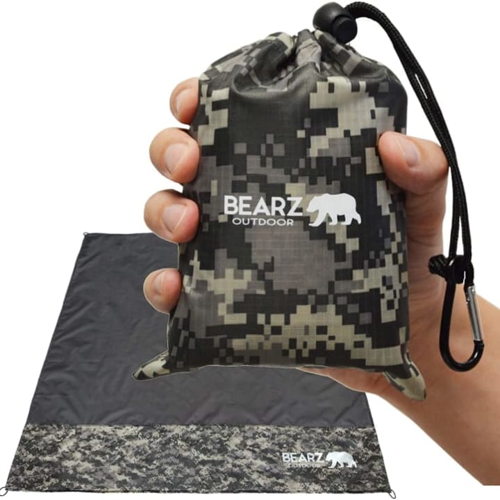 Close-up of a BEARZ Outdoor Blanket in camo print held by hand.