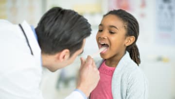 A doctor checks a young girl for swollen tonsils.