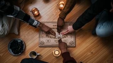 Friends consult a Ouija board during a séance.