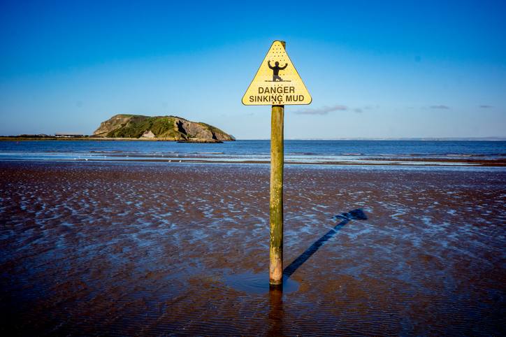 A triangular yellow sign warning "Danger Sinking Mud" in a river delta in Somerset, England.