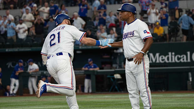 A baseball player in a white uniform that says "21" running past a man in a white uniform as they slap hands.