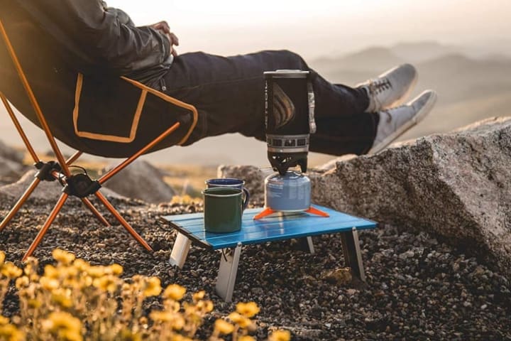 Person using a Trekology Personal Beach Table in nature with a mug