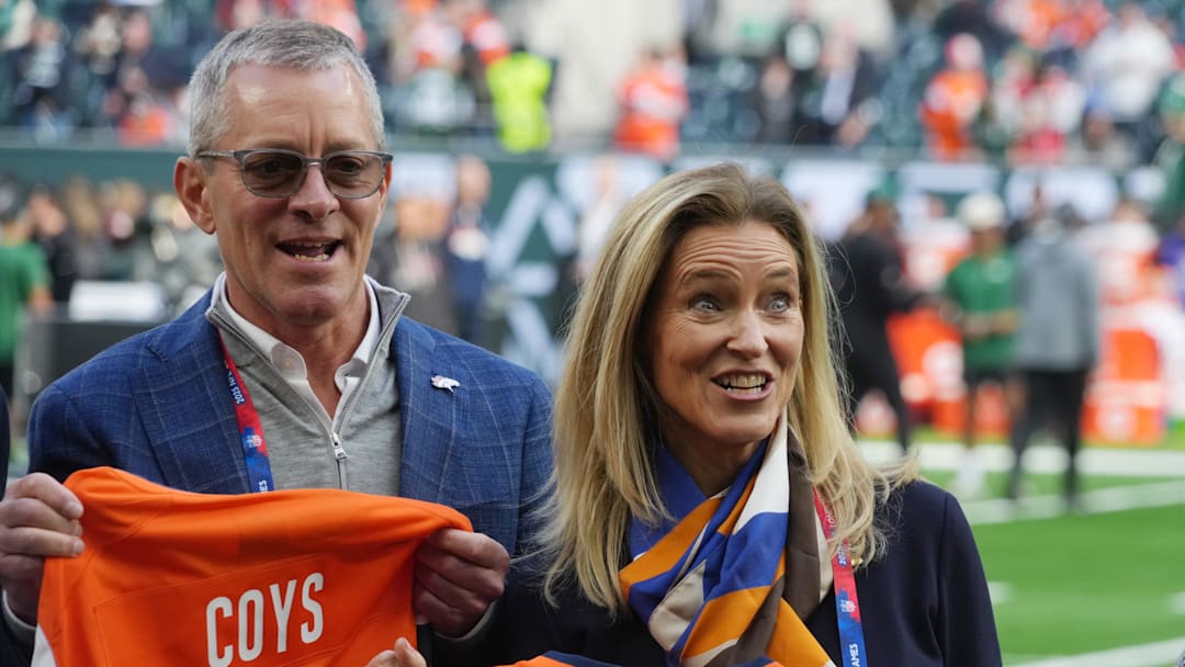 Oct 12, 2025; Tottenham, United Kingdom; Denver Broncos co-owners Greg Penner and Claire Walton Penner pose with jerseys before an NFL International Series game against the New York Jets at Tottenham Hotspur Stadium. Mandatory Credit: Kirby Lee-Imagn Images Oct 12, 2025; Tottenham, United Kingdom; Denver Broncos co-owners Greg Penner and Claire Walton Penner pose with jerseys before an NFL International Series game against the New York Jets at Tottenham Hotspur Stadium. Mandatory Credit: Kirby Lee-Imagn Images