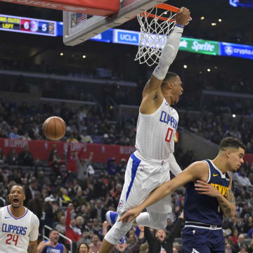 Apr 4, 2024; Los Angeles, California, USA;  Los Angeles Clippers guard Russell Westbrook (0) hangs on the rim after a dunk over Denver Nuggets forward Michael Porter Jr. (1) in the first half at Crypto.com Arena. 