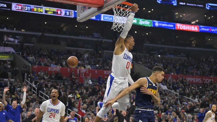 Apr 4, 2024; Los Angeles, California, USA;  Los Angeles Clippers guard Russell Westbrook (0) hangs on the rim after a dunk over Denver Nuggets forward Michael Porter Jr. (1) in the first half at Crypto.com Arena. 