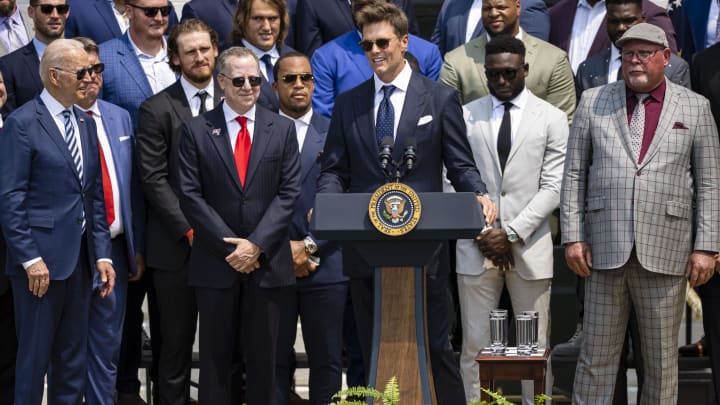 Jul 20, 2021; Washington, DC, USA; Tampa Bay Buccaneers quarterback Tom Brady speaks at the podium as President Joe Biden (left) and Buccaneers owner Bryan Glazer (middle left) and Buccaneers head coach Bruce Arians (right) look on during a ceremony on the South Lawn of the White House to honor the team for their Super Bowl LV Championship. Mandatory Credit: Scott Taetsch-USA TODAY Sports