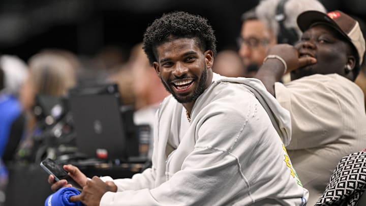 Sanders laughs as he watches a game between the Dallas Mavericks and the Denver Nuggets. 