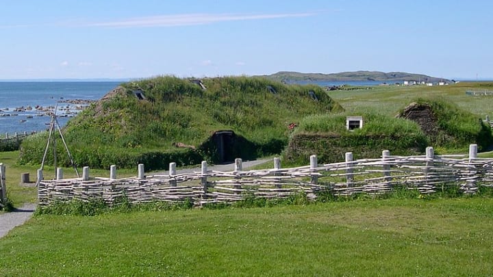 Recreated Viking sod houses behind a wooden fence at L'Anse aux Meadows in Newfoundland, Canada.
