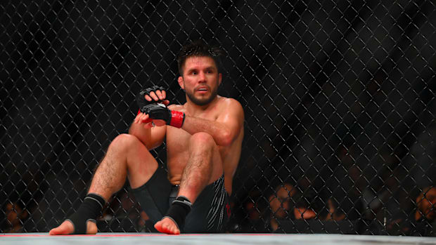 Henry Cejudo (red gloves) sits down after being poked in the eye by Song Yadong (blue gloves) in a bantamweight bout
