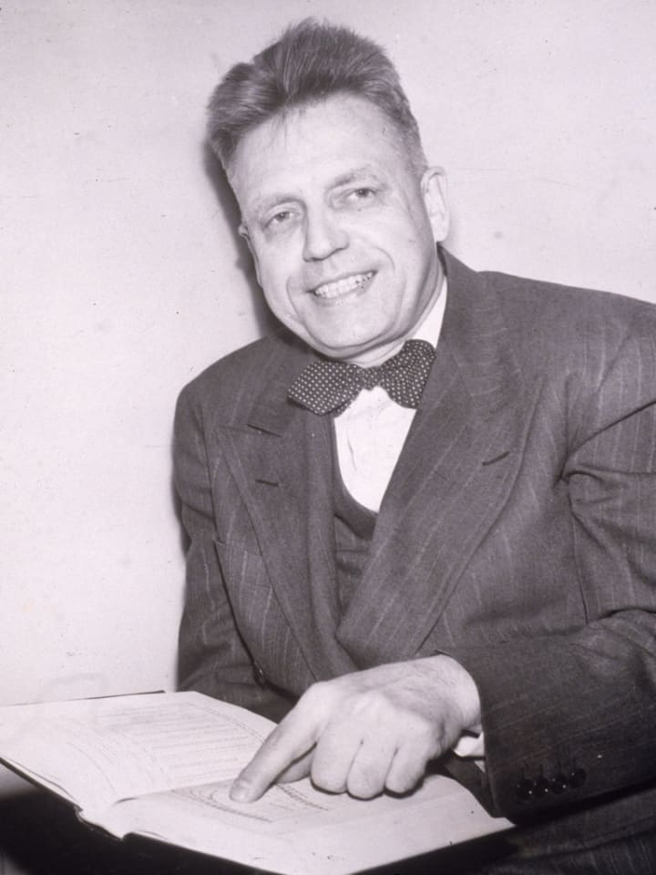 Alfred Kinsey smiling in a polka-dotted bow tie as he points to a passage in a book