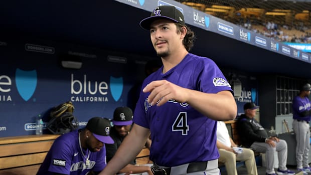Colorado Rockies player Michael Toglia walks around the dugoutin a purple jersey and black hat.