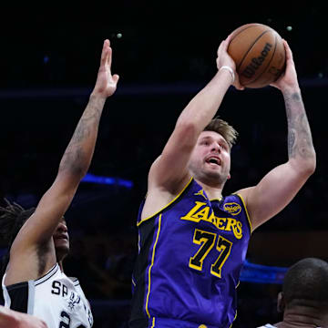 Mar 17, 2025; Los Angeles, California, USA; Los Angeles Lakers guard Luka Doncic (77) shoots the ball against San Antonio Spurs guard Devin Vassell (24) anda center Bismack Biyombo (18) in the first half at Crypto.com Arena. Mandatory Credit: Kirby Lee-Imagn Images