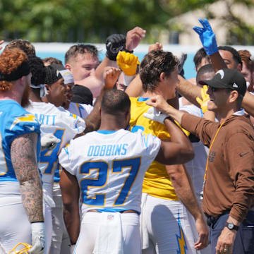 Jun 13, 2024; Costa Mesa, CA, USA; Los Angeles Chargers coach Jim Harbaugh joins hands in a huddle with tight end Donald Parham Jr. (89), running back J.K. Dobbins (27), quarterback Justin Herbert (10) and receiver Ladd McConkey (15) during minicamp at the Hoag Performance Center. Mandatory Credit: Kirby Lee-Imagn Images