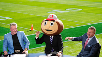 Jan 1, 2025; Pasadena, California, USA; Lee Corso (center) wears a Buckeyes mascot head  as Pat McAfee (left) and Kirk Herbstreit (right) watch at Rose Bowl Stadium. Mandatory Credit: Kirby Lee-Imagn Images