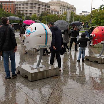 Fans pose with large helmets of the Washington Commanders, 2025 NFL Madrid Game and the Miami Dolphins at Palacio de Cibeles. 