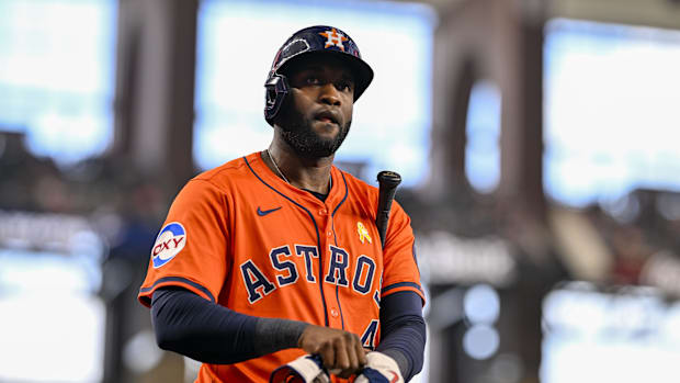 A baseball player in an orange uniform that says "Astros" with a dark helmet and baseball bat.