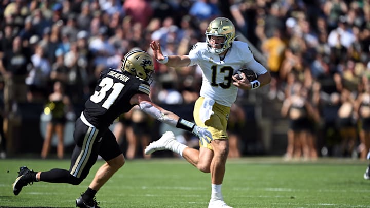 Sep 14, 2024; West Lafayette, Indiana, USA; Notre Dame Fighting Irish quarterback Riley Leonard (13) reaches out to stiff arm Purdue Boilermakers defensive back Dillon Thieneman (31) during the first quarter at Ross-Ade Stadium. Mandatory Credit: Marc Lebryk-Imagn Images