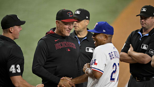 A man in a white uniform and blue hat shaking hands with men in black clothing on the green baseball field.
