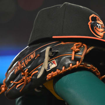 A Baltimore Orioles hat and glove rest on the dugout rail
