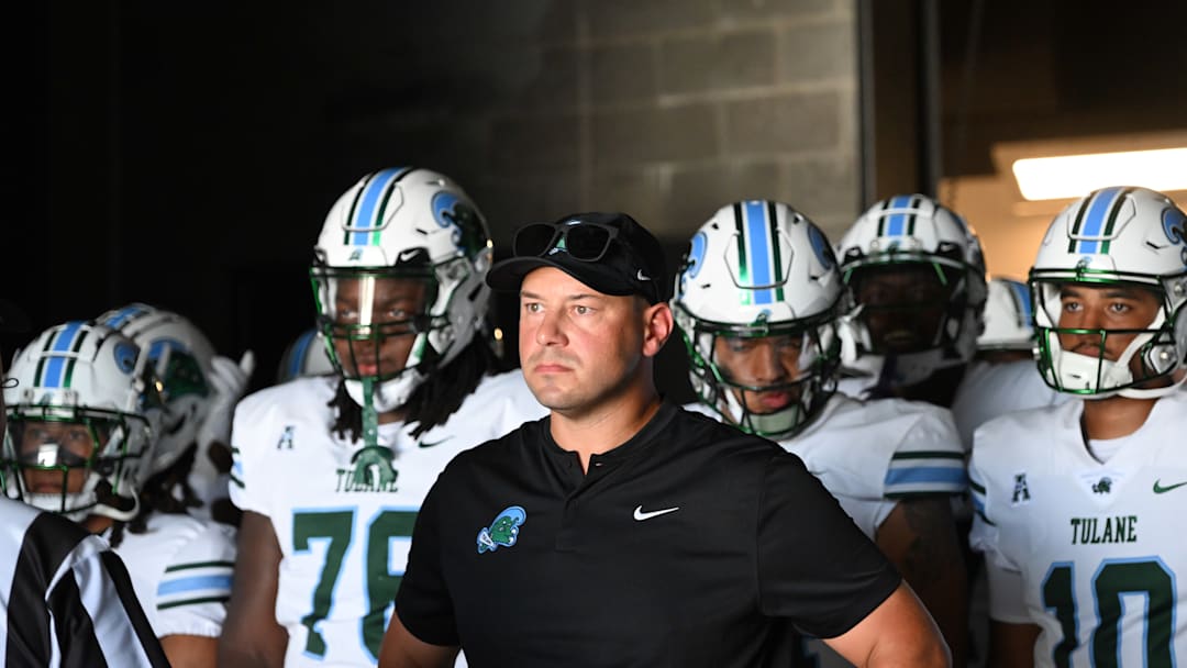 Tulane Green Wave college football coach Jon Sumrall walks out tunnel with his players behind him.