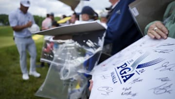 May 14, 2024; Louisville, Kentucky, USA; A fan holds a tournament flag as Bryson DeChambeau signs autographs.