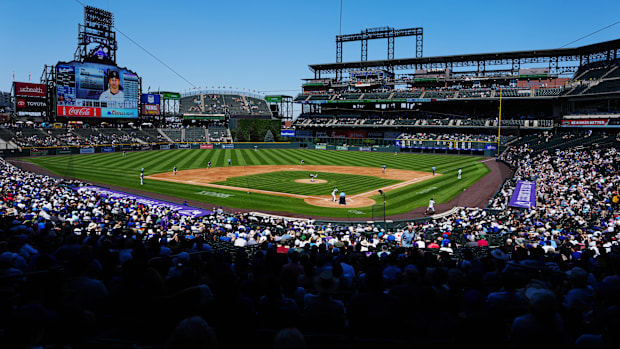 General view from behind home plate of Coors Field, showing fans in attendance and players on the field. 